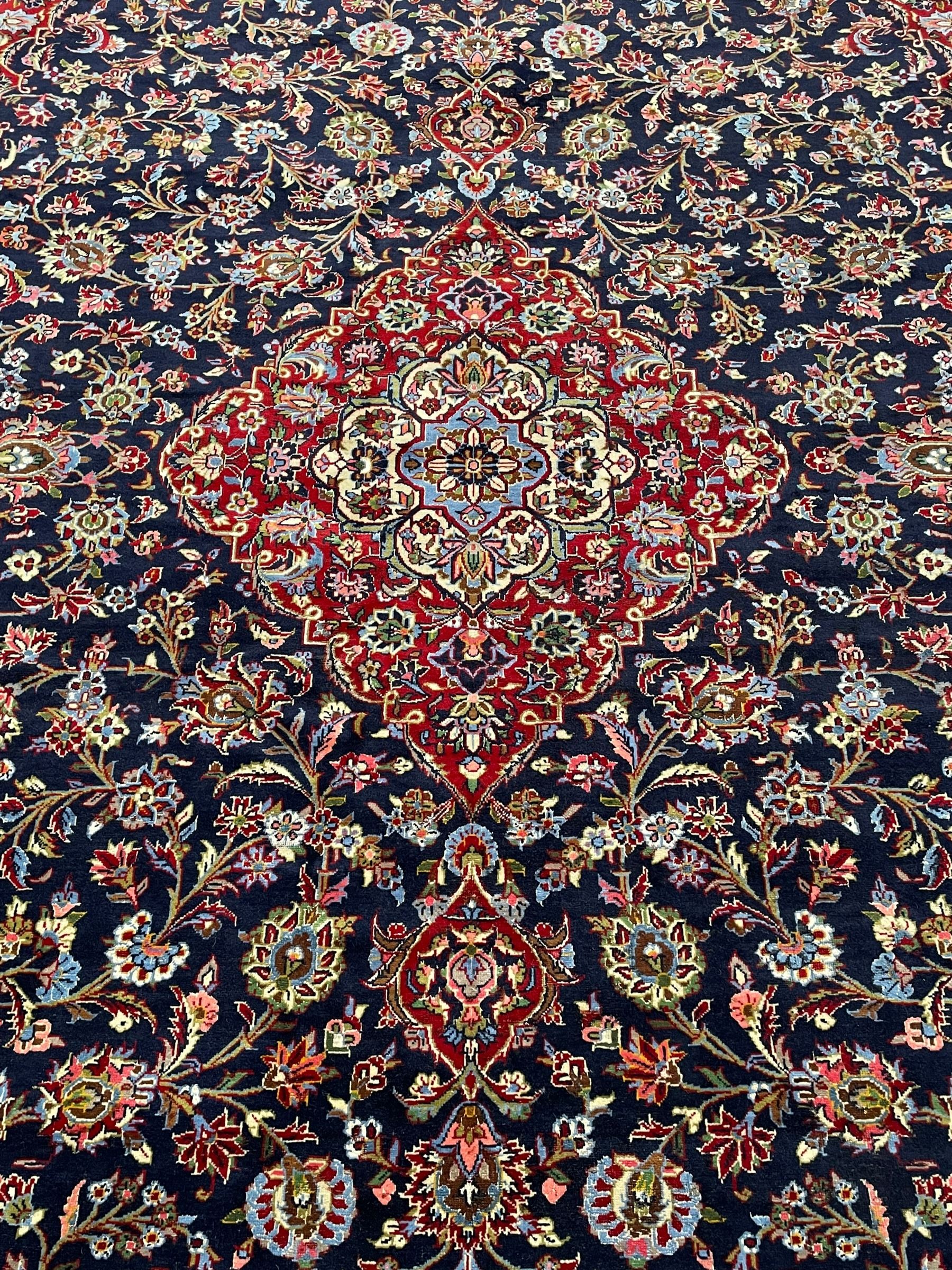 Persian Kashan indigo ground carpet, central floral pattern medallion surrounded by a densely decorated field depicting trailing branches with leaves and palmettes, scrolling border decorated with stylised plant motifs, within floral pattern guard stripes 