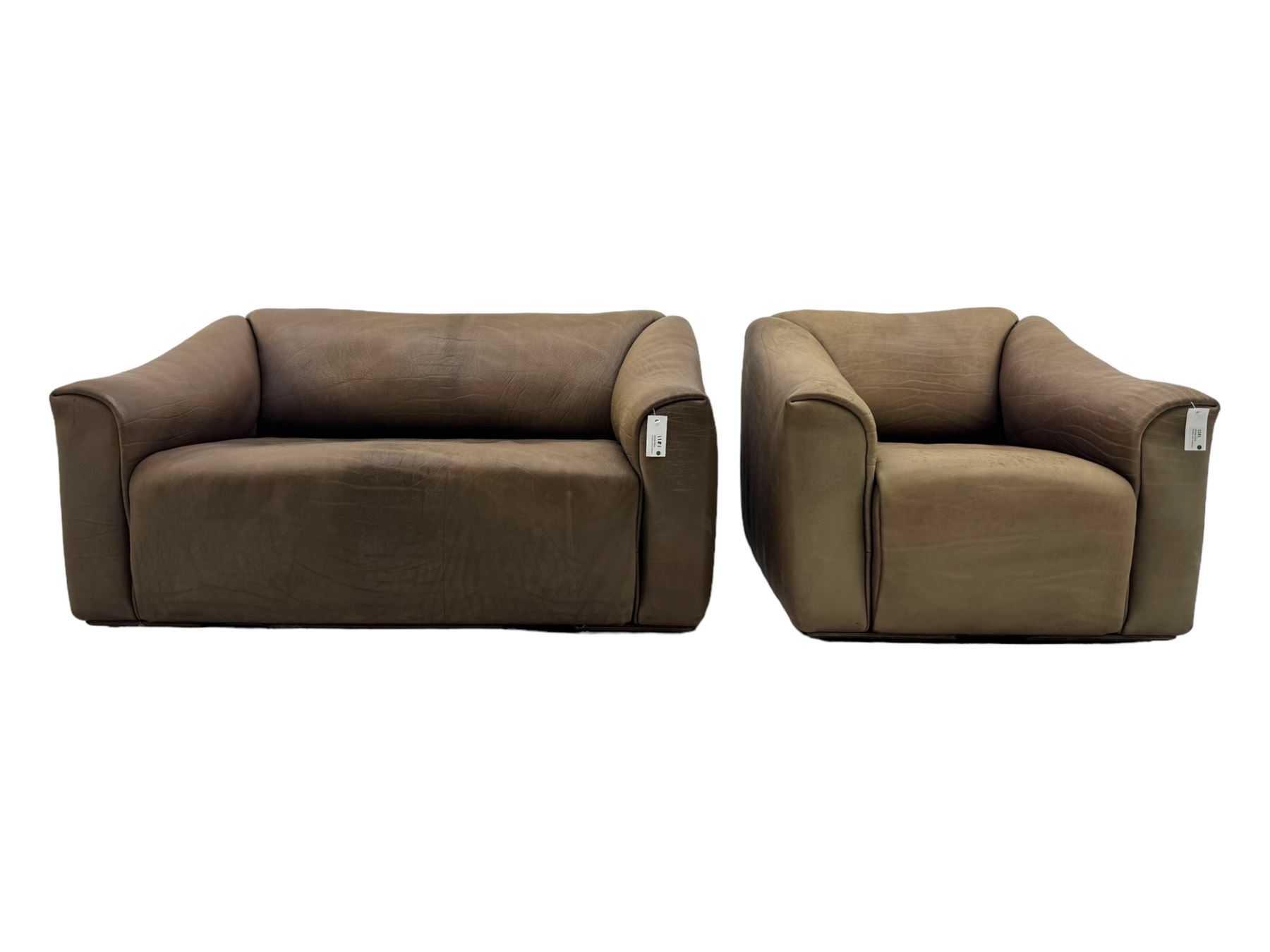 Mid-20th century two seater sofa, upholstered in soft brown leather with visible patina, curved arms and low back, on concealed supports (W138cm, D86cm, H72cm); matching armchair (W84cm, D86cm, H72cm)