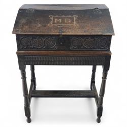 18th century carved oak Bible box on stand, the sloping lid with incised initials ‘MD’ and iron strap hinges, the front carved with stylised leaf and scroll panels enclosing central iron lockplate, on stand with gadrooned frieze, turned legs and plain stretchers
