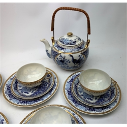 A Japanese eggshell porcelain teaset, comprising six teacups each with Geisha lithophane panel, six saucers, six side plates, teapot with woven carry handle, twin handled sucrier and milk jug, each decorated with blue floral and peacock pattern and heightened with gilt. 