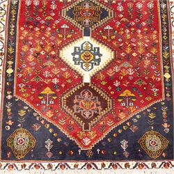South West Persian hand-knotted Qashgai runner, madder-red field with a central column of linked diamond medallions in tones of indigo, ochre, ivory, and green, surrounded by stylized floral and boteh motifs within a cream border of angular vines and serrated devices, with cotton fringe ends   