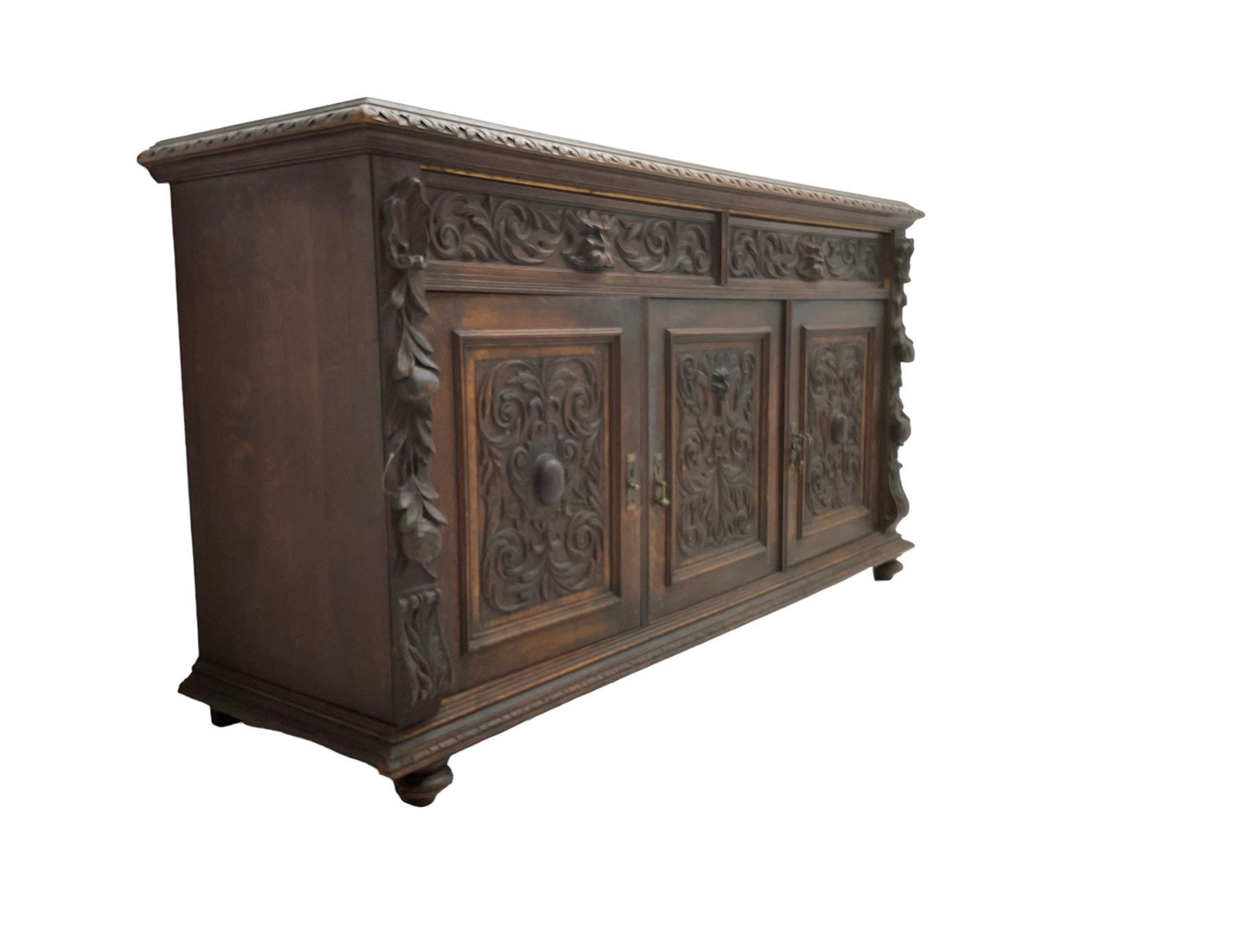 Victorian heavily carved oak sideboard, the moulded top carved with foliate decoration to the edge, fitted with two drawers and three cupboards, the drawer fronts carved with green man mask handles and scrolling foliage, the panelled doors carved with interlacing foliage, on turned compressed bun feet