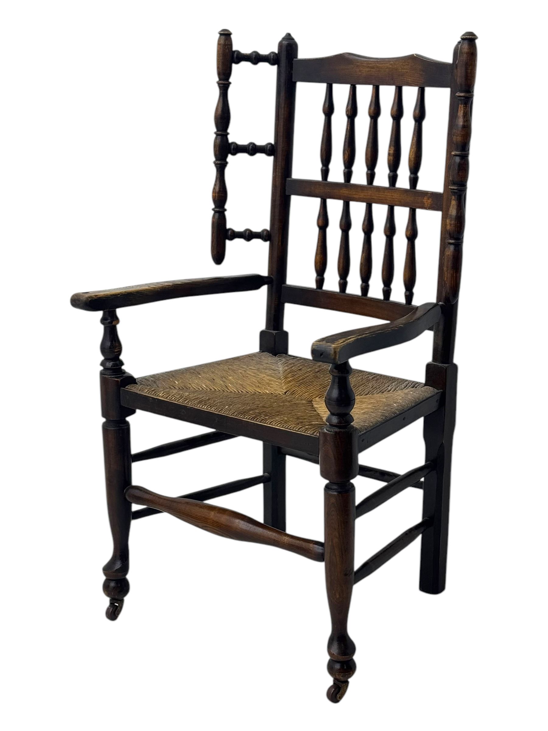 Early 19th century ash armchair, the back with winged spindles extending from a shaped top rail, above a splat of two rows of vertical spindles, with curved arms and a rush seat, raised on turned supports united by double stretchers terminating in castors