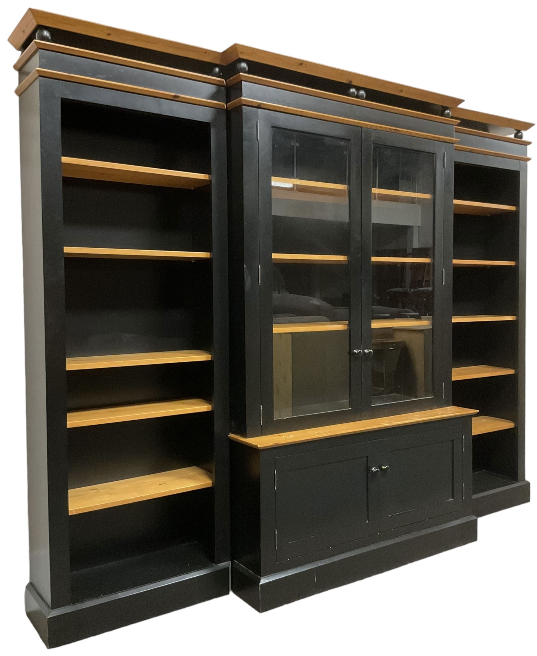 Contemporary polished pine and black finish break-front bookcase, projecting cornice over globular mounts, central cabinet enclosed by two glazed doors over double panelled cupboard, flanked by adjustable shelves, on plinth base