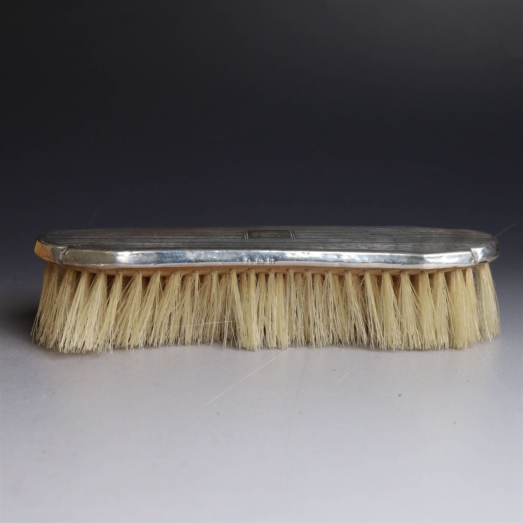 Five silver mounted dressing table items, including 1920s mirror and hairbrush set, with engraved initial to reverse, pair of clothes brushes with engraved initials and engine turned decoration and an oval clothes brush, all hallmarked 