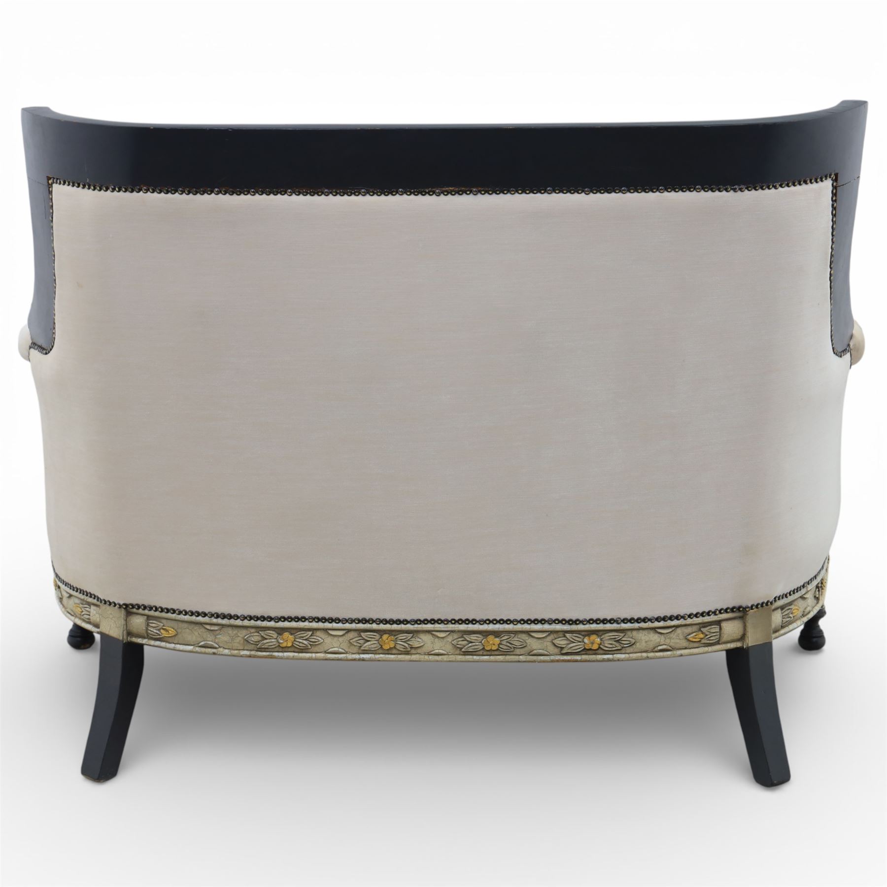 20th century Louis XVI style settee, upholstered in cream fabric with buttoned back and arms, and plain seat cushions, the shaped and black painted frame with entwined foliate detail and gilt flower heads, upon column legs with bun feet