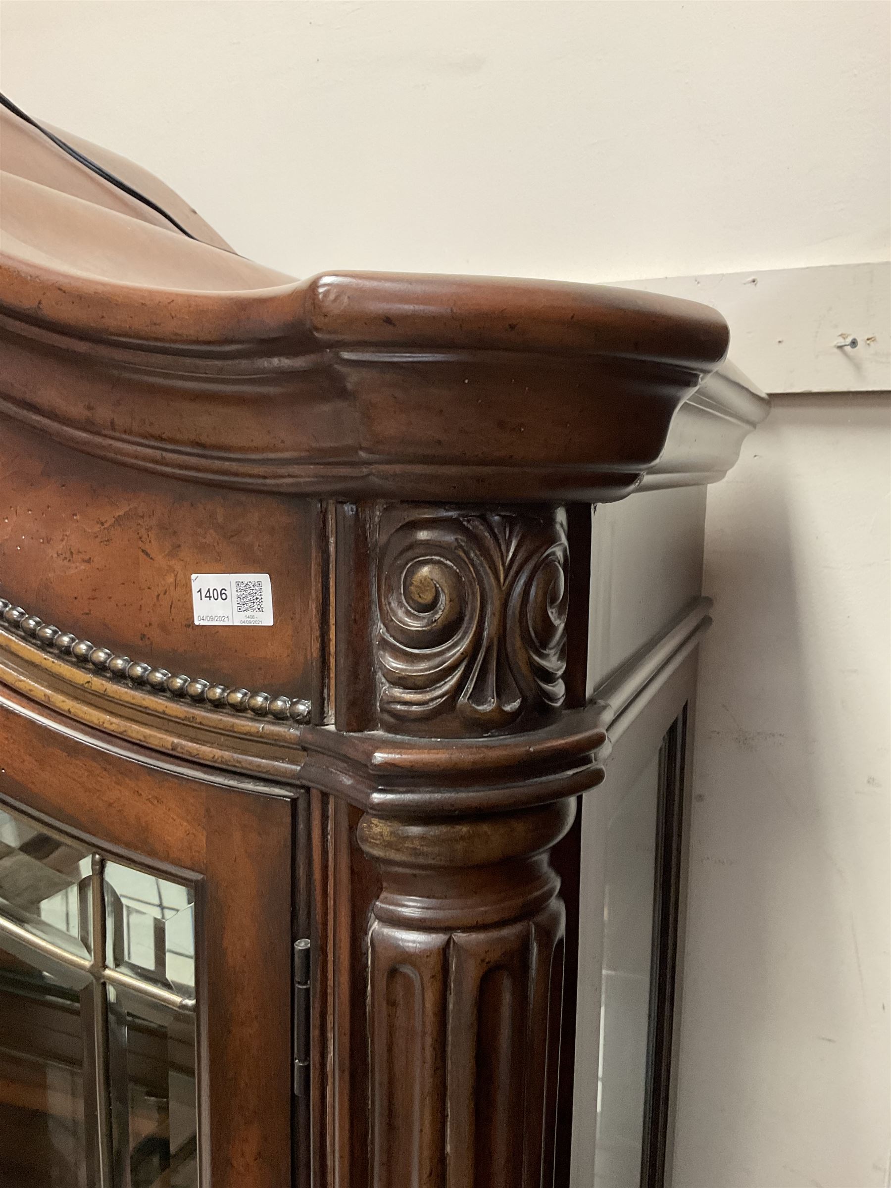 Kevin Charles American walnut display cabinet, illuminated interior, shell carved pediment above four bevel edge doors enclosing six glazed shelves above one central long drawer flanked by two short drawers, above three cupboards, carved bracket supports 