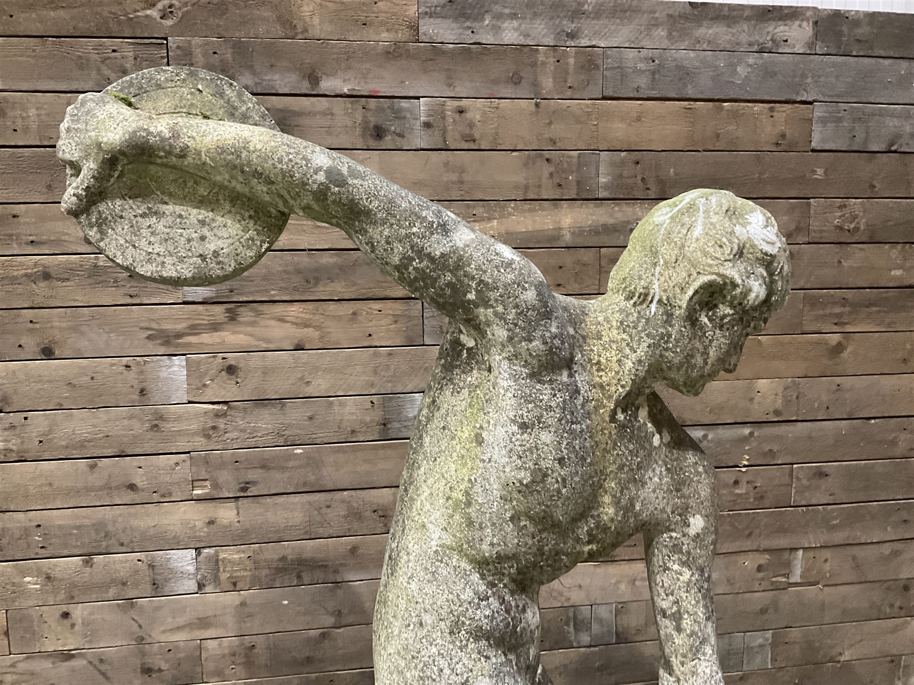 Life-size weathered cast stone Greek Discus Athlete, seated on rectangular slab raised on associated architectural plinth