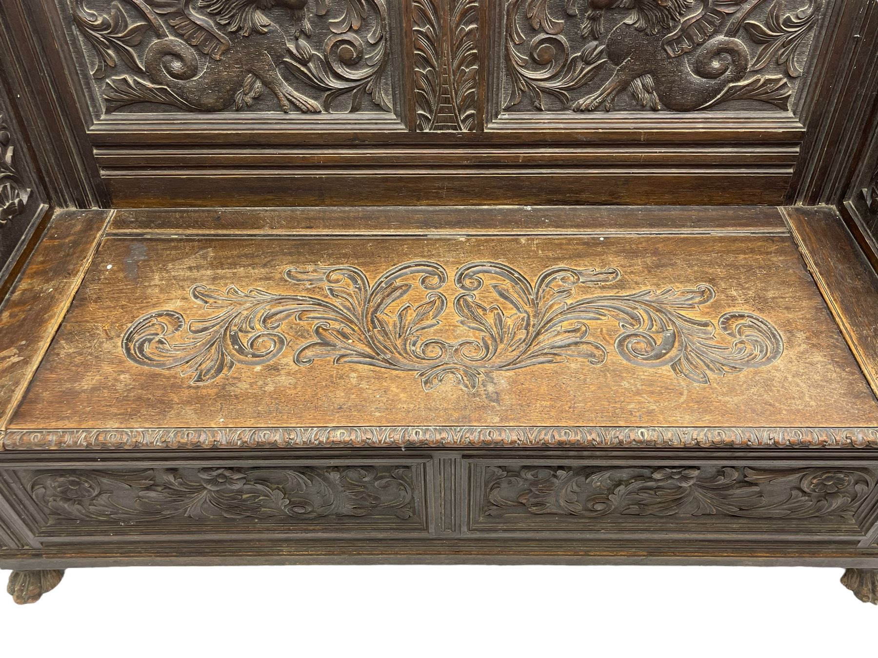 19th century oak hall bench, dentil cresting rail over moulded frame with panelled back carved with fire-breathing mythical beasts and central acanthus leaf motif, scroll carved down-sweeping arms carved with grotesque masks with scrolled foliage and shells, hinged box seat carved with scrolling foliage over panelled front with further carved foliage decoration, on paw carved front feet 