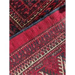 Afghan Bokhara red ground carpet, the field decorated with four rows of Gul motifs interspersed with Hac motifs, the border with lattice pattern panels within small geometric guard stripes, geometric patterned end panels