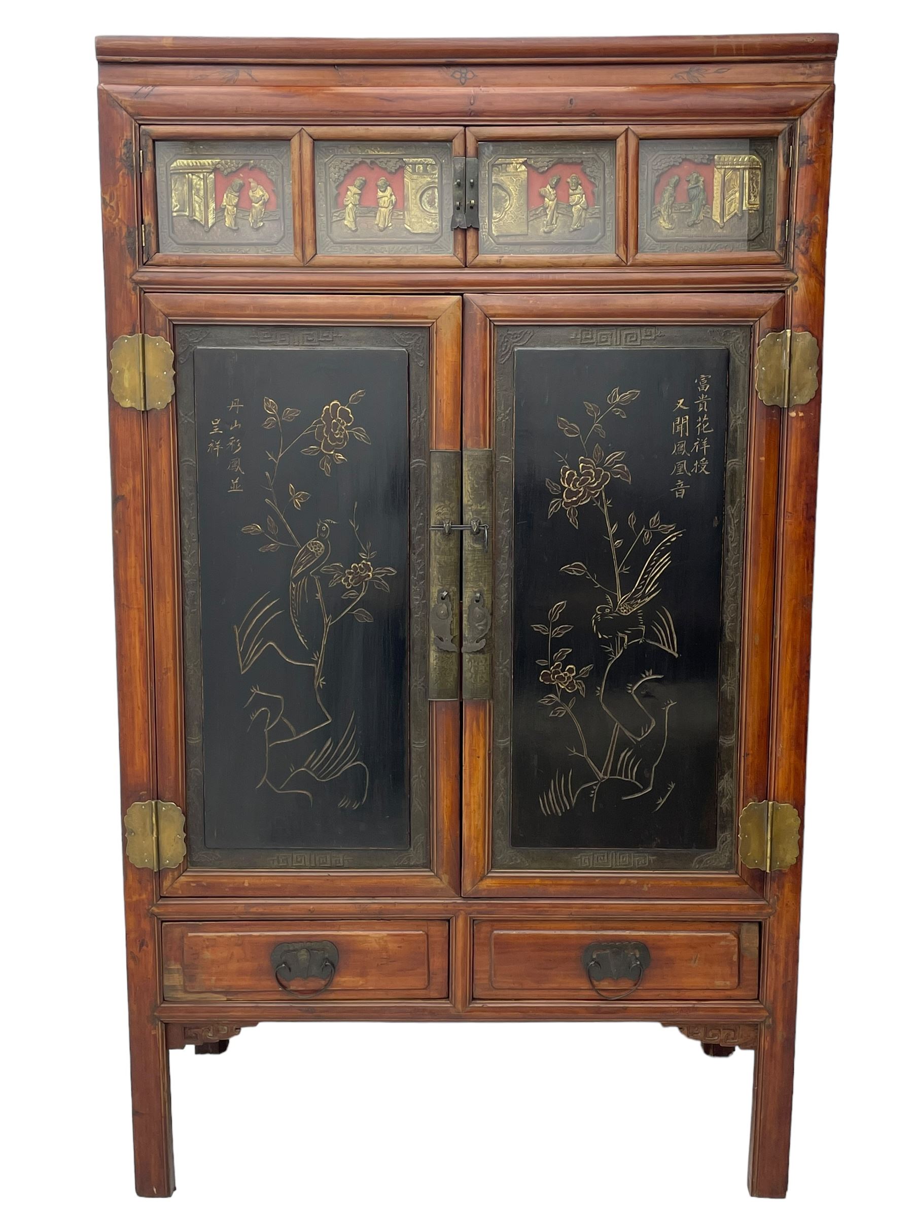 Late 19th century Chinese Qing dynasty red and black lacquered wood cabinet,  Fujianese province, upper cupboard enclosed by two doors with relief carved and gilt panels depicting figures behind glass, the large cupboard enclosed by two panelled doors carved with trailing foliate branches and birds, inscribed with Chinese characters, to the left ‘The red mountains are in the shape of Phoenixes and appear auspicious’ and to the right, ‘Wealth and honour are given by flowers and I hear the sound of the phoenix', fitted with two drawers, on square supports with carved brackets 