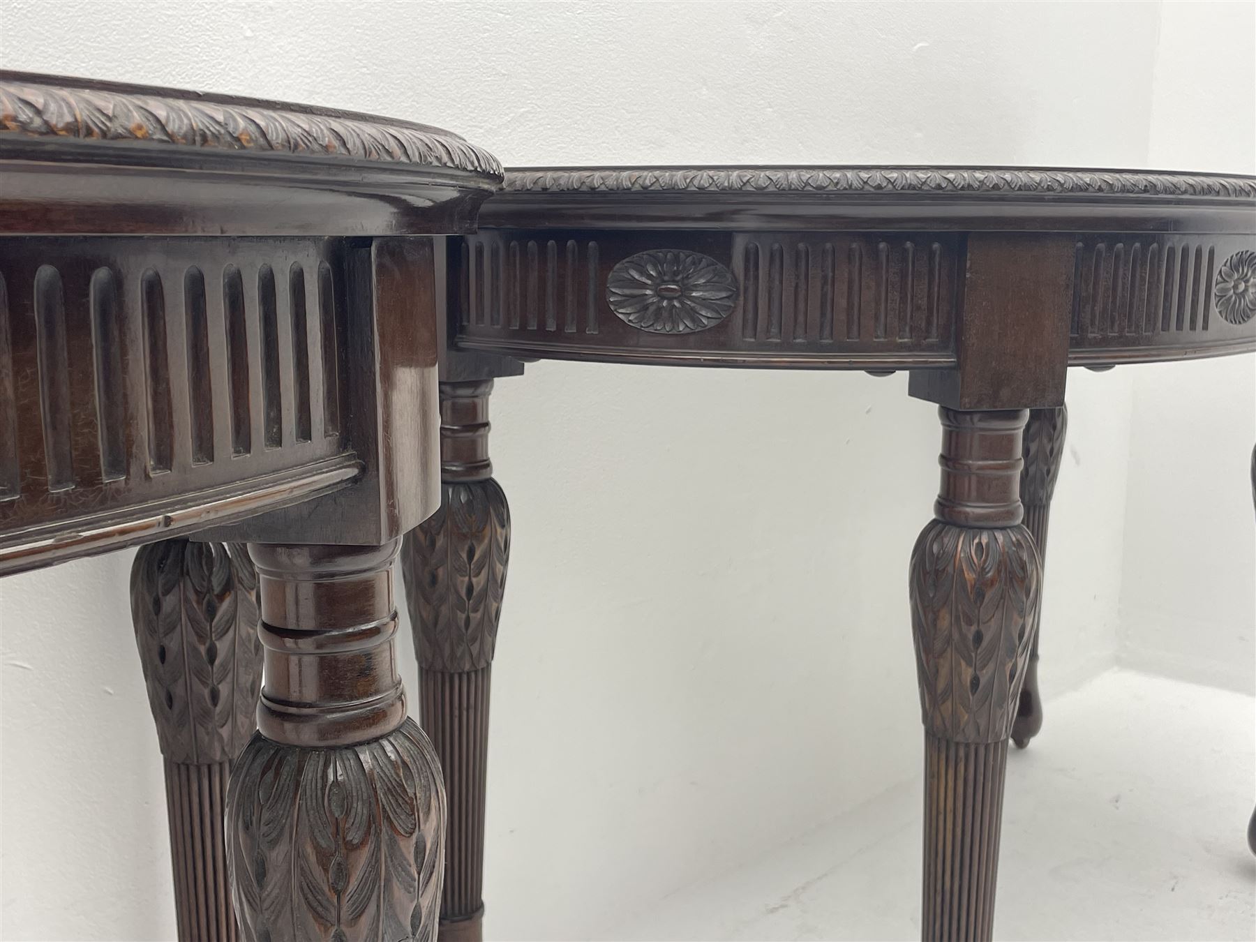 Pair early 20th century Hepplewhite style mahogany D-end console tables, the curved top with foliate carved edge, fluted frieze rails carved with flower heads, turned and reeded acanthus supports with recessed castors