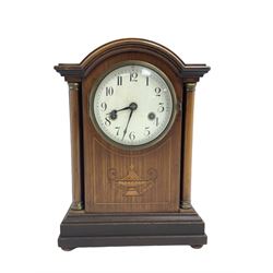 German - Edwardian 8-day mahogany mantle clock c1910, with a break arch pediment and two recessed columns with brass capitals, front decorated with an inlaid motif and satinwood stringing, on a stepped base with bun feet, white enamel dial with Arabic numerals, minute track and steel spade hands, two train countwheel striking movement striking the hours and half hours on a coiled gong. With pendulum & Key.