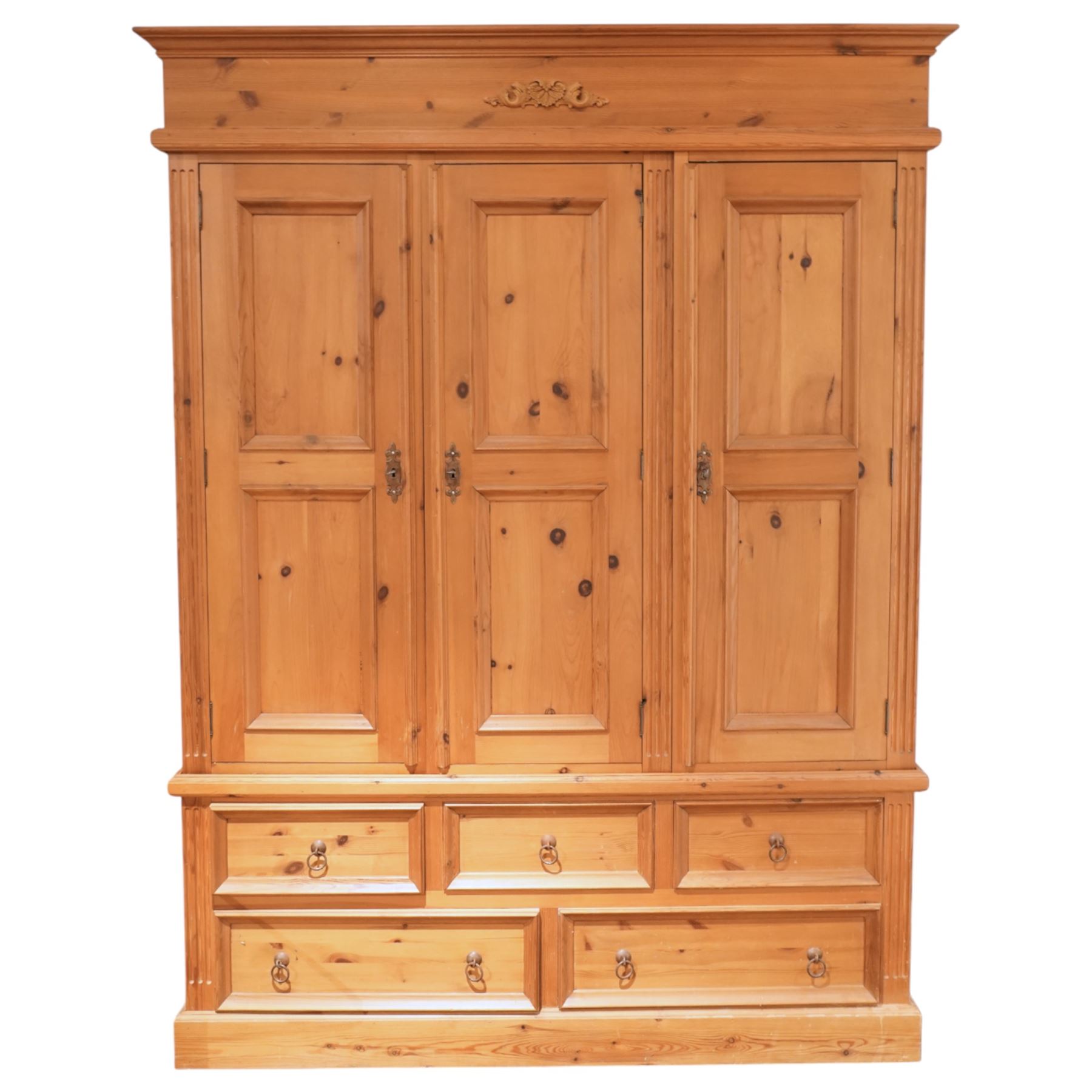 20th century pine wardrobe with drawer base, moulded cornice over three fielded panel cupboard doors enclosing hanging compartments, the base fitted with three short and two long drawers with brass ring handles, raised on a plinth base