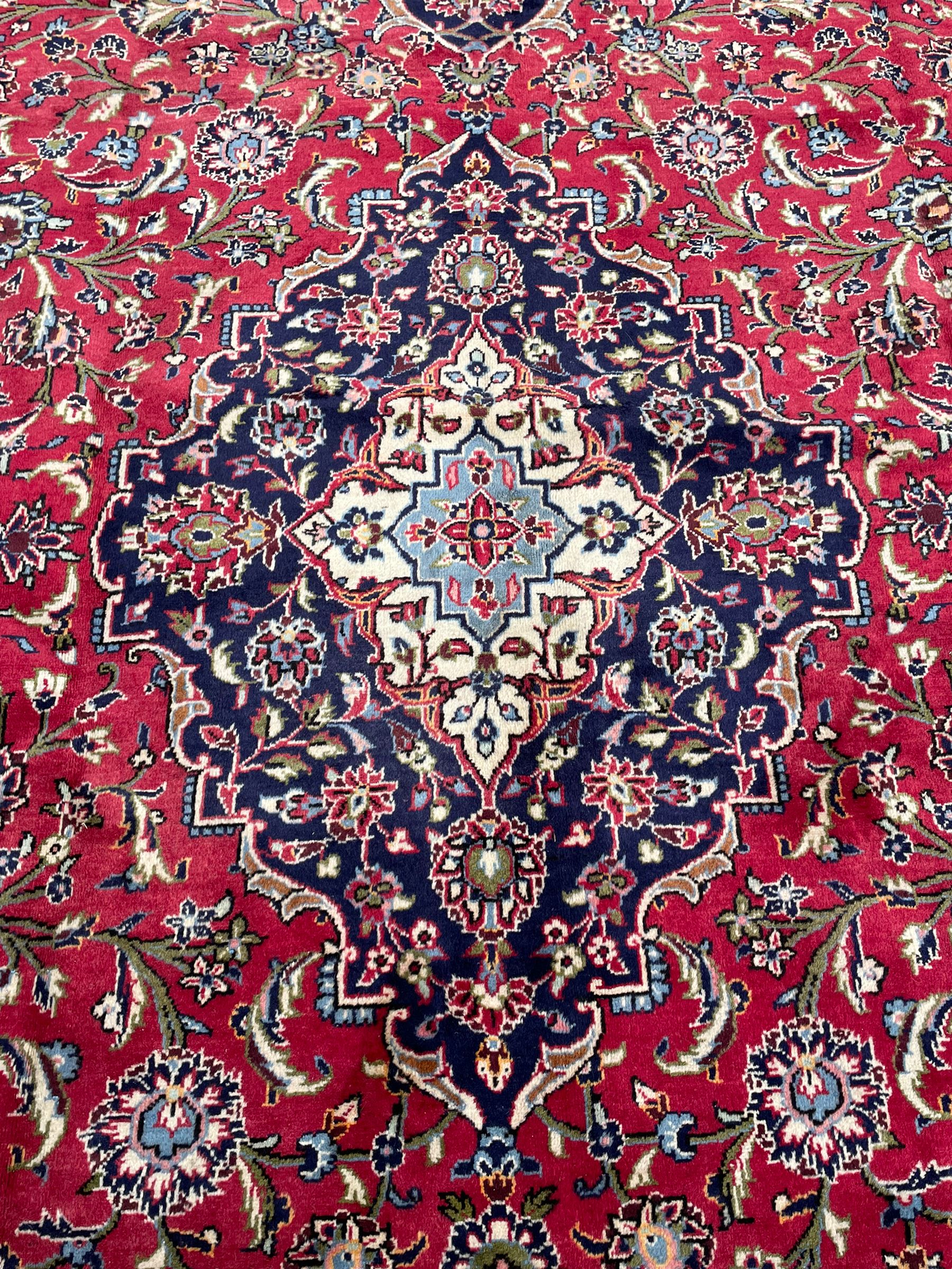 Central Persian Kashan crimson ground carpet, central  floral pole medallion with matching spandrels within a field of scrolling palmette motifs and foliage, the heavily banded indigo border with repeating plant motifs interlaced with scrolled branches