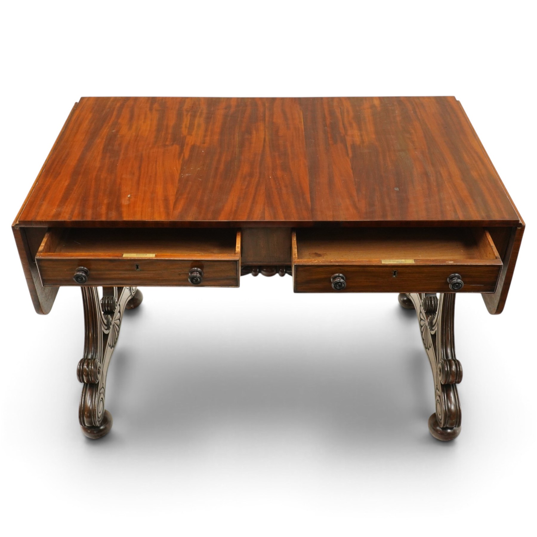 Fine 19th century figured mahogany sofa table, the rectangular twin drop-leaf top with rounded corners above two cock-beaded frieze drawers with opposing faux drawers, fitted with turned handles, raised on twin reeded and C-scroll-carved end supports with palmette-carved platform bases and compressed bun feet, united by a turned and foliate-carved stretcher