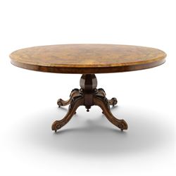 Victorian figured and burr walnut loo table, oval book-matched veneer top with moulded edge, over a turned octagonal pedestal terminating to four splayed supports with flowerhead carved knees and scroll feet with castors