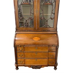 Large and impressive late 19th century Irish mahogany secretaire bookcase, moulded sloped arch dentil pediment decorated with central carved mask surrounded by linen festoons and trailing bellflowers, canted and fluted uprights with carved acanthus leaf upper and lower brackets, enclosed by two astragal glazed doors in the form of trophies with twist ribbon carved mouldings, inlaid with fanned spandrels and trailing leaf painted satinwood band, cylinder roll top inlaid with central fan motif and fanned spandrels, pull-out action revealing stepped fitted interior, central tambour roll cupboard flanked by two Composite pilasters and a combination of drawers and pigeon holes, fitted with three break-front drawers, matched canted and fluted corners with acanthus leaf carvings, on square tapering and fluted spade feet