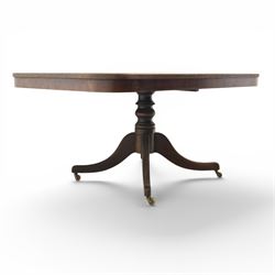 Regency mahogany tilt-top dining table, crossbanded rounded rectangular top, raised on a splayed base, terminating in brass castors