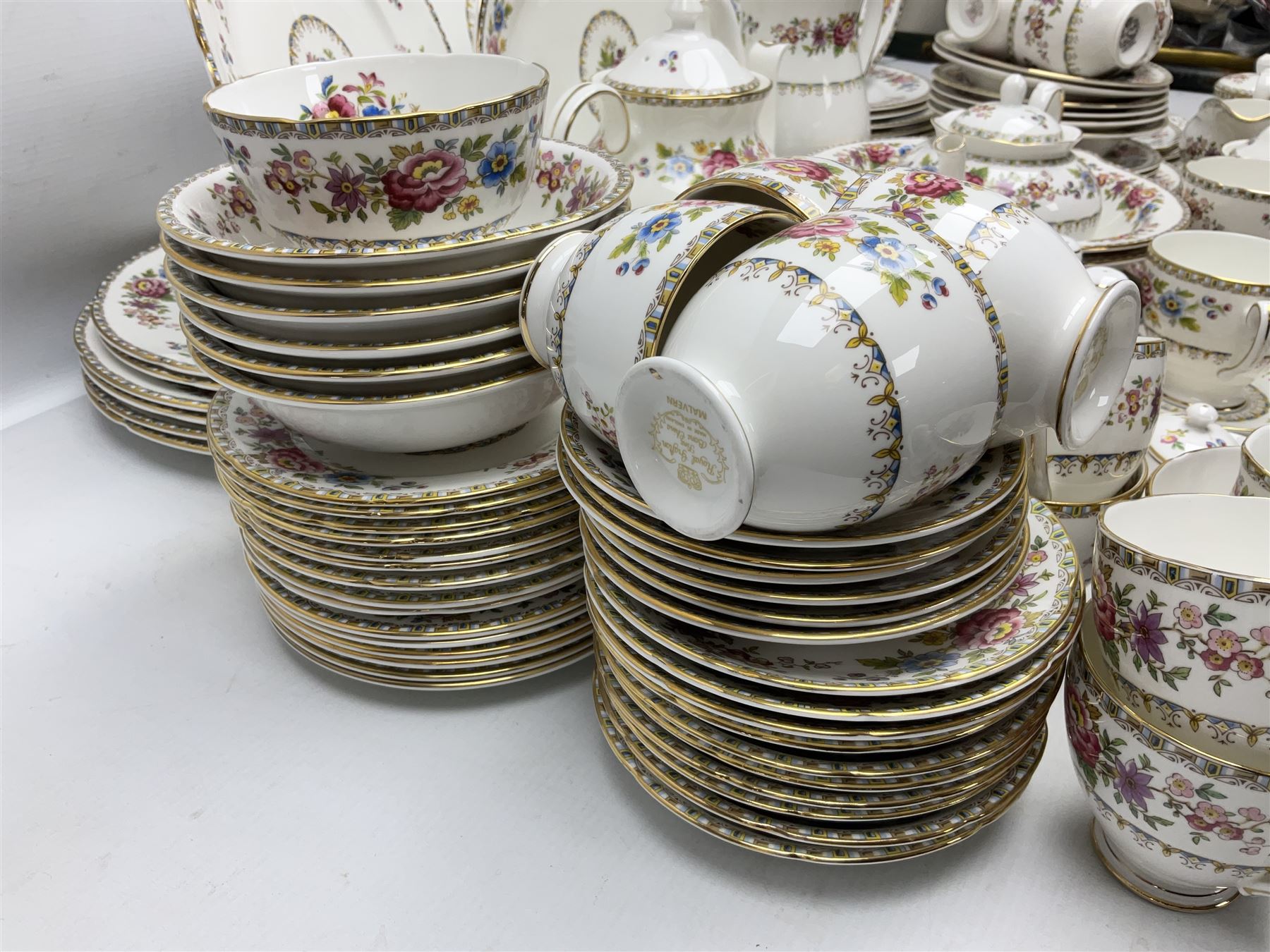 Extensive Royal Grafton Malvern pattern tea and dinner wares, comprising twelve dinner plates, six smaller plates, coffee pot, two teapots, two cake plates, eight teacups and ten saucers, six coffee cups and six saucers, two open sucriers, twin handled lidded sucrier, jug, lidded mustard pot and condiment jar, lidded tureen, two circular twin handled vegetable tureens, sauce boat and stand, oval and circular serving plates, salt and pepper shakers, breakfast cup and two saucers, further large cup and saucer, eighteen tea plates of various shapes, six side plates, six cereal bowls and six further bowls, shell dish and dish of square form, fork and knife, together with a hallmarked silver condiment spoon