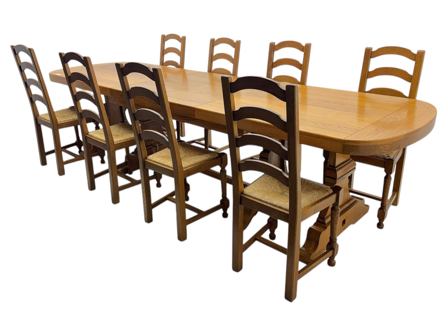 Oak extending dining table with elegant scrolled shaped double pedestal base and scrolled feet; together with a set of eight ladder back chairs with rush seats ((9) table closed 228x95x79cm chairs 106x38x44cm 