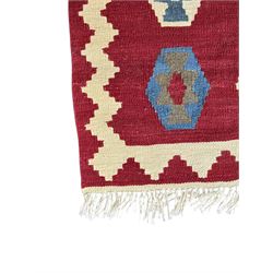 Handwoven wool Kilim rug of rectangular form with cream fringe, the red ground decorated with repeated multicoloured hexagonal medallions within a cream stepped border