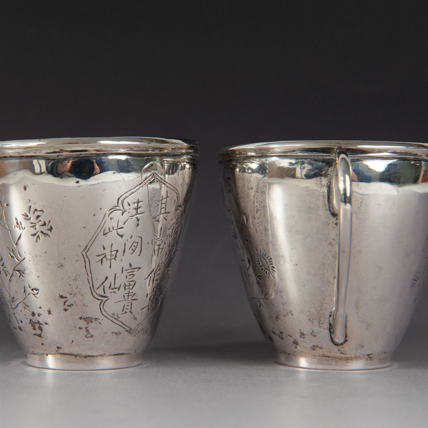 Pair of Chinese export silver teacups, both decorated with character marks, one with floral decoration, the other decorated with a bird within bamboo branches, both with indistinct maker's marks beneath, H6cm