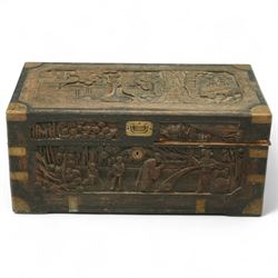 Early 20th century Chinese brass bound camphor wood coffer, rectangular form, the hinged lid and sides deeply relief carved with figures in landscape scenes within geometric borders, fitted with brass corner mounts and recessed carry handles