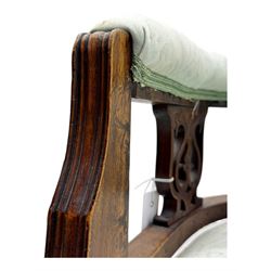 Late Victorian carved mahogany open armchair, the shaped back with fluted upholstered panel and padded arms above pierced scroll carved side supports, over a broad upholstered seat, on turned front supports