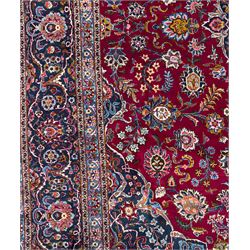 Central Persian Kashan hand-knotted carpet, madder red field with an intricate design of scrolling vines, palmettes, and rosettes with a central lobbed medallion with pendant motifs in shades of blue and ivory, and spandrels all within a blue-ground border of palmettes and flowerheads between multiple guard borders, 450cm x 335cm 