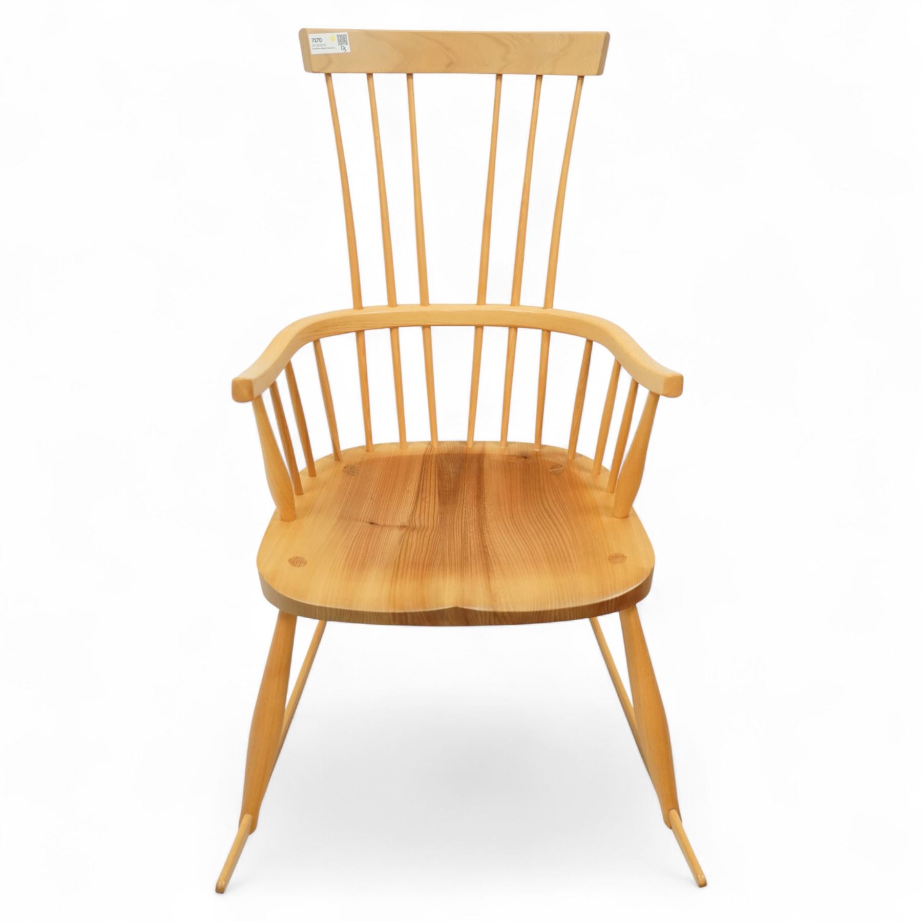 Mid 20th century Windsor ash rocking armchair, in the manner of Ercol, with curved cresting rail above nine stick spindles, shaped and chamfered paddle arms, figured shaped seat, raised on turned legs joined by twin side stretchers and mounted on curved rockers