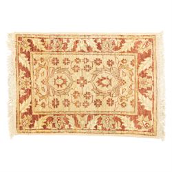 Lot of three Indo-Ziegler style wool rugs, comprising one with central floral medallion and palmette border, and two matching examples with scrolling vine and flowerhead motifs on a deep red field, each with decorative border in soft gold tones (60cm x 85cm) (65cm x 115cm)