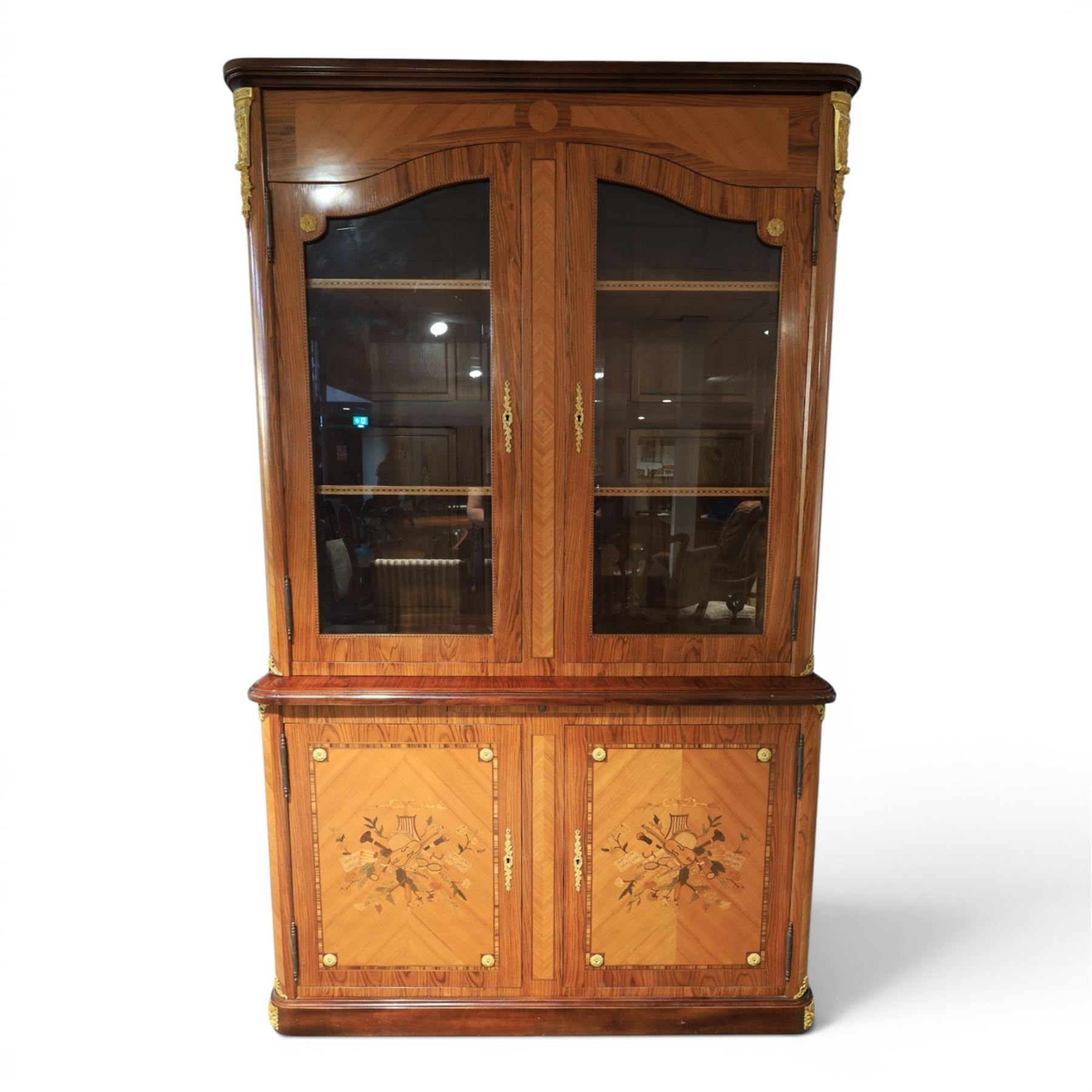 French style marquetry display bookcase, with twin glazed upper doors enclosing shelves, over a cupboard base inlaid with musical instruments and foliate decoration, the interior fitted with mirrored cupboard doors and a pull-out shelf, with gilt metal mounts and banding