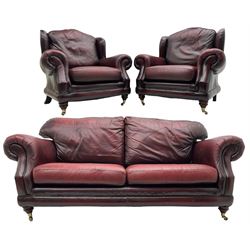 Thomas Lloyd - three-piece lounge suite, comprising of traditional shape two seat sofa (W190cm H80cm) and a pair of wingback armchairs (W100cm H91cm), each with rolled arms over turned supports with brass castors, upholstered in oxblood red leather