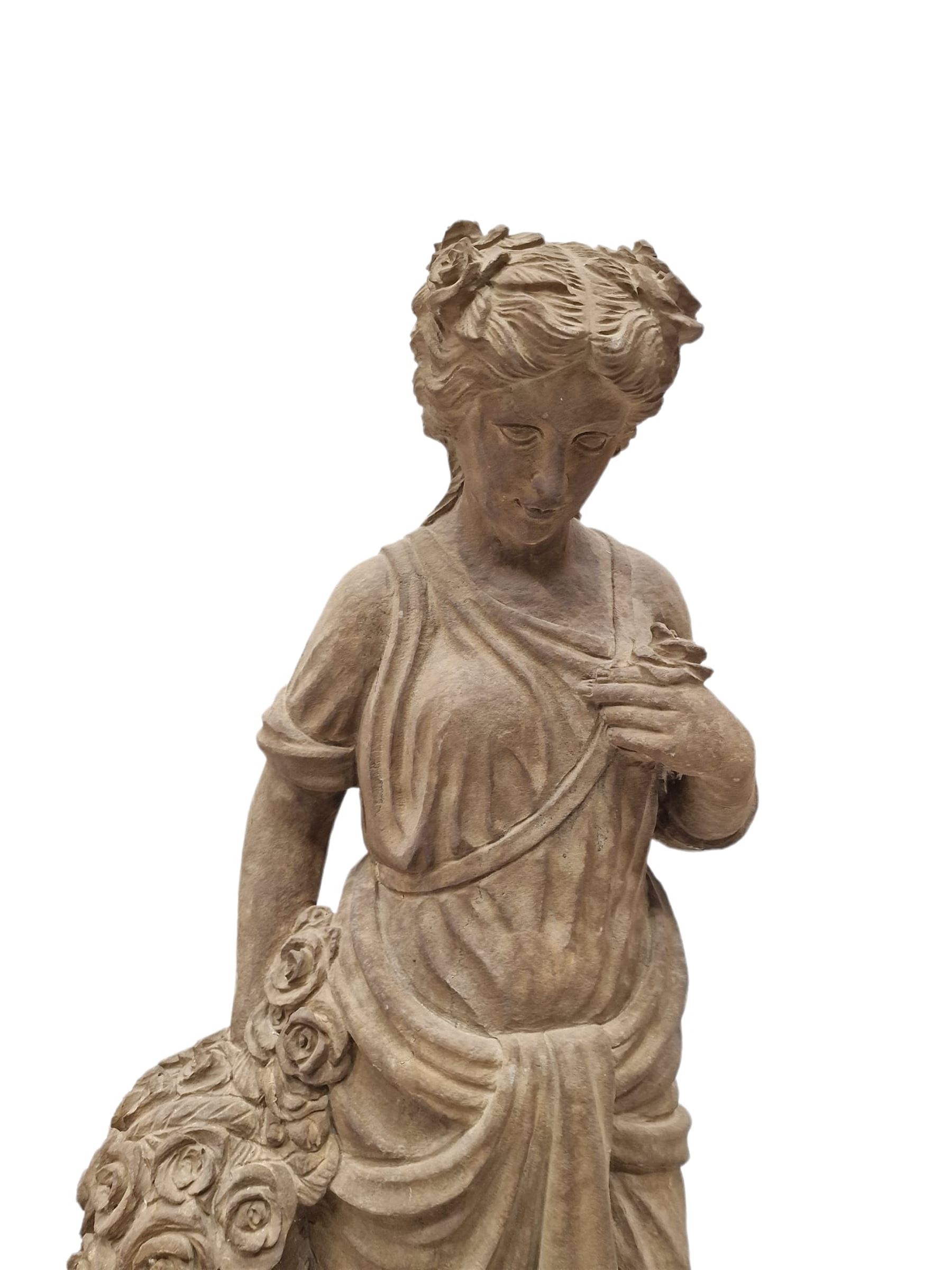 Hand carved stone Neoclassical figure of the Roman goddess Flora, her hair pinned with roses, draped in a toga, holding a basket of flowers in her right hand, raised on a stepped square plinth base 