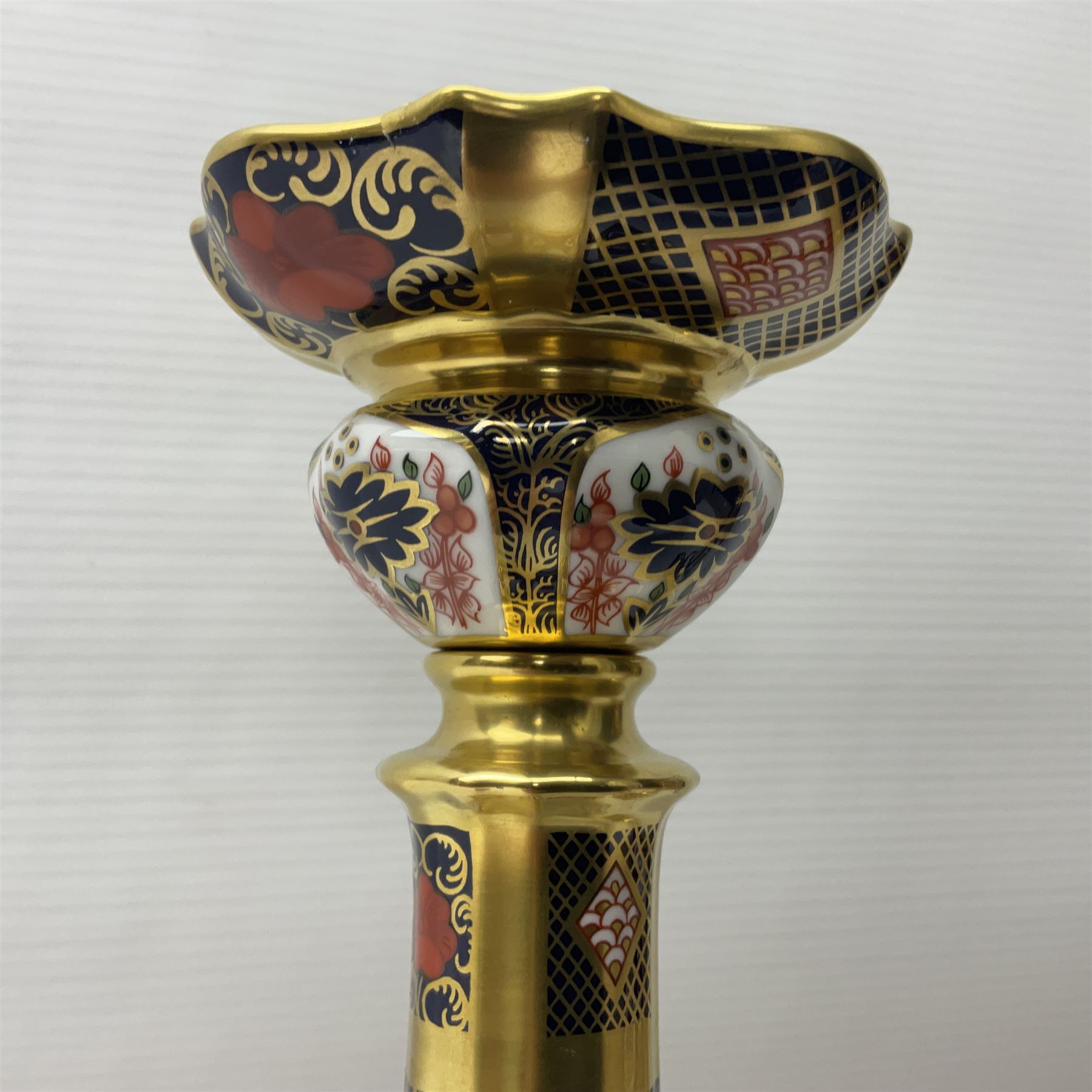 Pair of modern Royal Crown Derby Old Imari 1128 pattern candlesticks, each with shaped drip tray affixed to squat socket, upon spreading stem and canted square base with gilt dolphin edges, with printed marks beneath including Roman numeral year cypher for 2003, H26.5cm, with original boxes