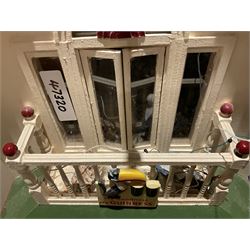 Seagull Pub - scratch-built wooden doll's house as a two-storey gable fronted public house painted in white green and maroon; the hinged front with ground floor veranda and window over opening to reveal two fully furnished rooms with dog-leg staircase and well stocked bar with bar-tender L31cm H62cm D37cm; together with Corner Shop and Dollies Pantry; a similarly painted scratch-built wooden two-storey flat-roofed doll's house as a well stocked ground floor grocery shop with stairs up to two further fully furnished rooms and more stairs giving access to a roof terrace L46cm H57cm D33cm (2)