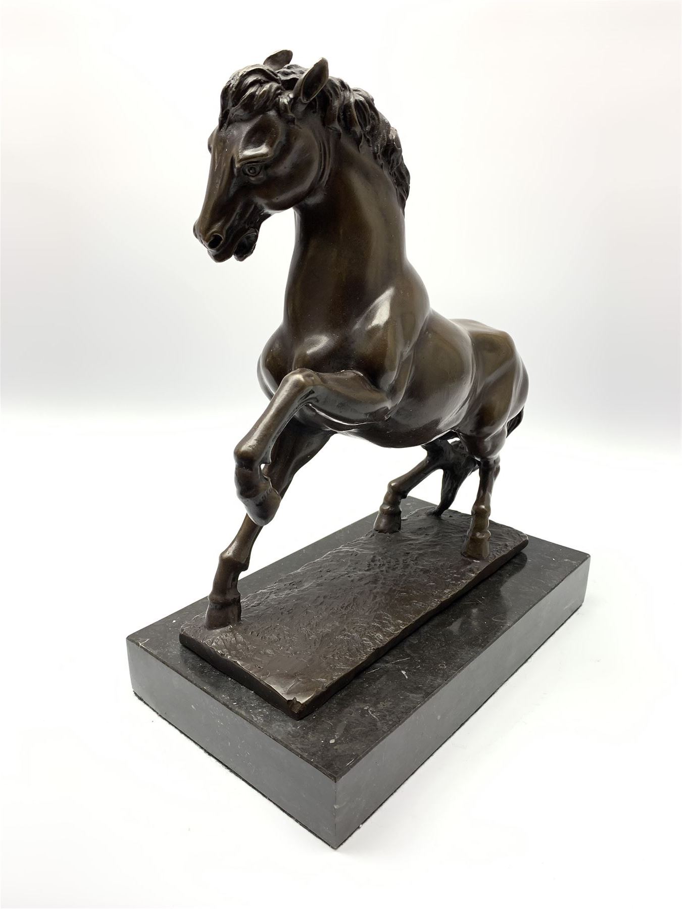 Bronze figure modelled as a prancing horse, upon a naturalistically modelled rectangular base, and black marble plinth, H34.5cm, L31cm