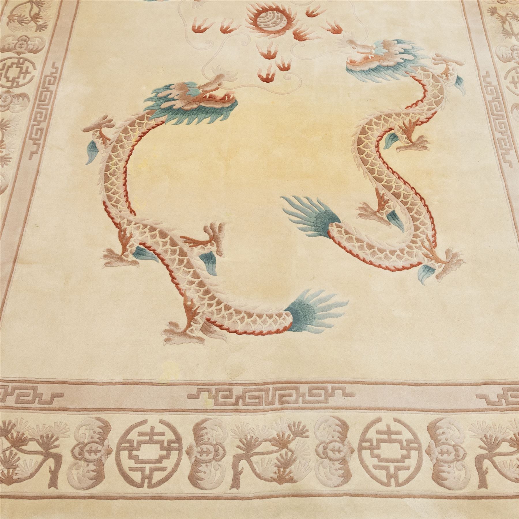 Late 20th century Chinese wool carpet, cream field with five stylized dragons arranged in a circular formation around a central flaming pearl motif, dragons depicted with elongated bodies and clawed feet amongst stylized cloud forms, enclosed within a narrow inner border and a wider outer border decorated with traditional Chinese motifs and symbols