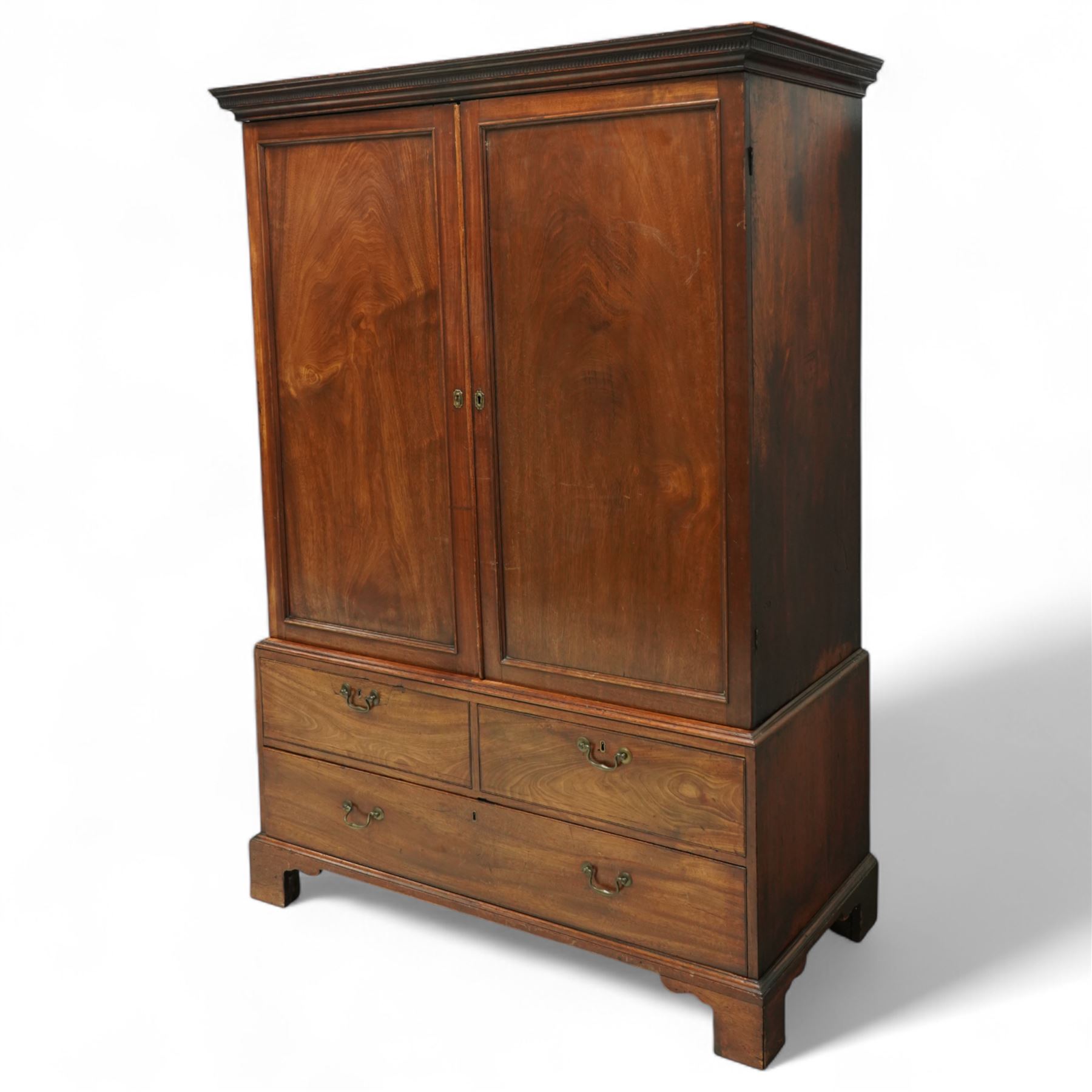 George III mahogany linen press, dentil moulded cornice over a pair of panelled doors enclosing a later fitted interior, lower section with two short over one long cockbeaded drawer, brass swan neck handles, shaped bracket feet