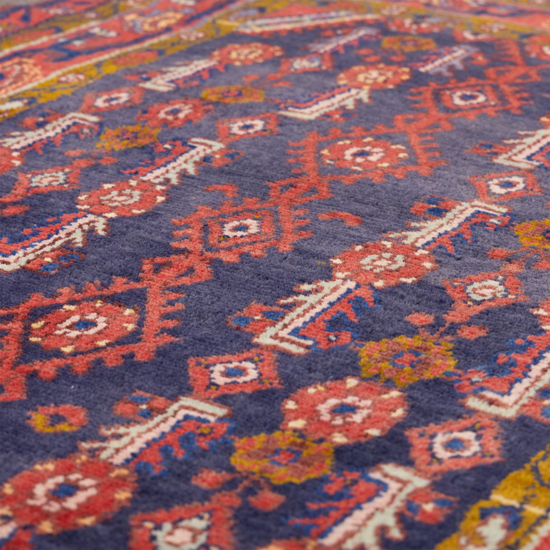 North West Persian Cirjan hand-knotted rug, indigo field decorated with vertical columns of stylized boteh, rosettes and diamond devices arranged in a repeating lattice and a chain of linked lozenges, enclosed by a mustard gold inner border and a principal border of madder ground, flanked by narrow guard stripes, with cotton fringe ends 