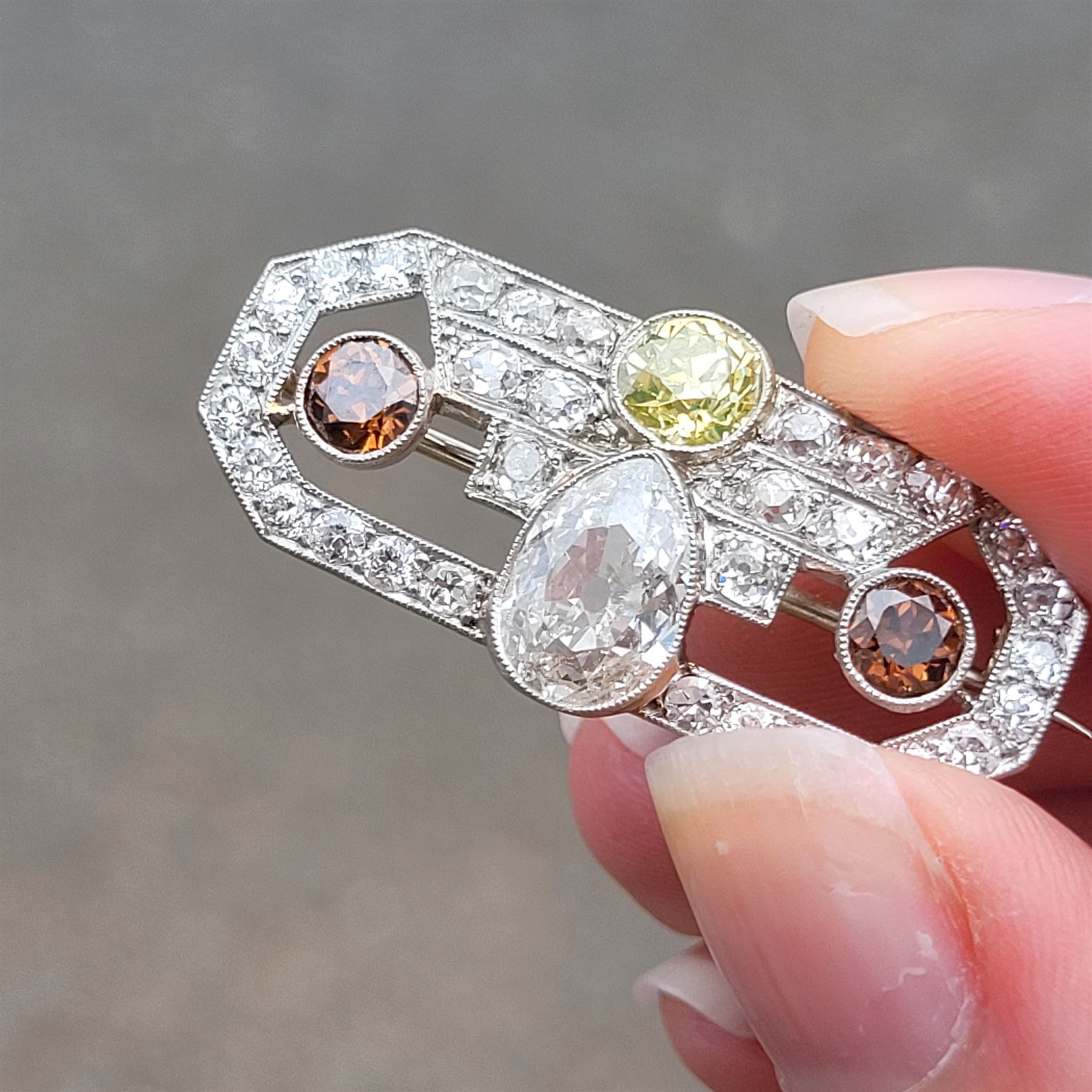 Early 20th century platinum diamond brooch, milgrain set with a pear cut faint brown diamond of approx 1.50 carat, an old cut fancy yellow / green diamond of approx 0.70 carat, and two old cut fancy orange / brown diamonds of approx 0.40 carat and 0.35 carat, surrounded by old cut white diamonds in an openwork setting, total white diamond weight approx 1.45 carat