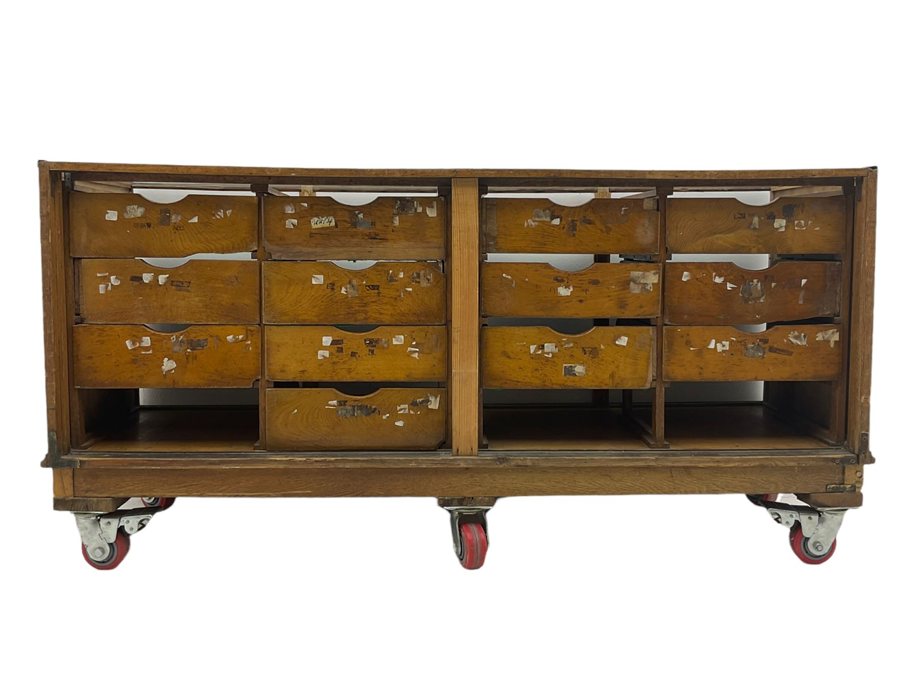 Early 20th century oak framed and glazed haberdashery / shop display cabinet, fitted with sixteen drawers (three missing), on later casters
