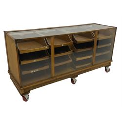 Early 20th century oak framed and glazed haberdashery / shop display cabinet, fitted with sixteen drawers (three missing), on later casters