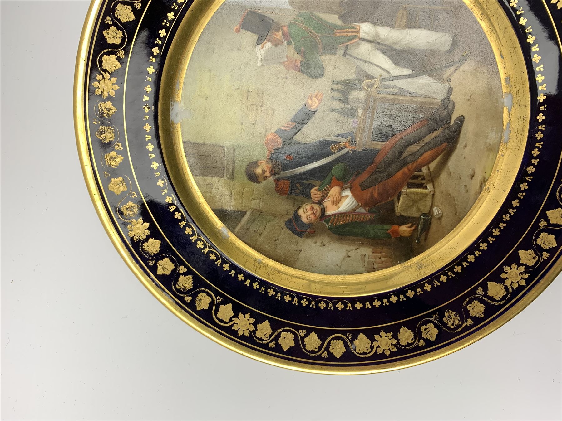 19th century Rihouet Paris porcelain cabinet plate, decorated with a central panel illustrating three French soldiers around a bottle laden table, one surveying a note, within a dark blue gilt detailed border, with French inscription verso, and red printed mark Rihouet Rue de la Paix A Paris and green fish mark, possibly for Perche, D23cm 



