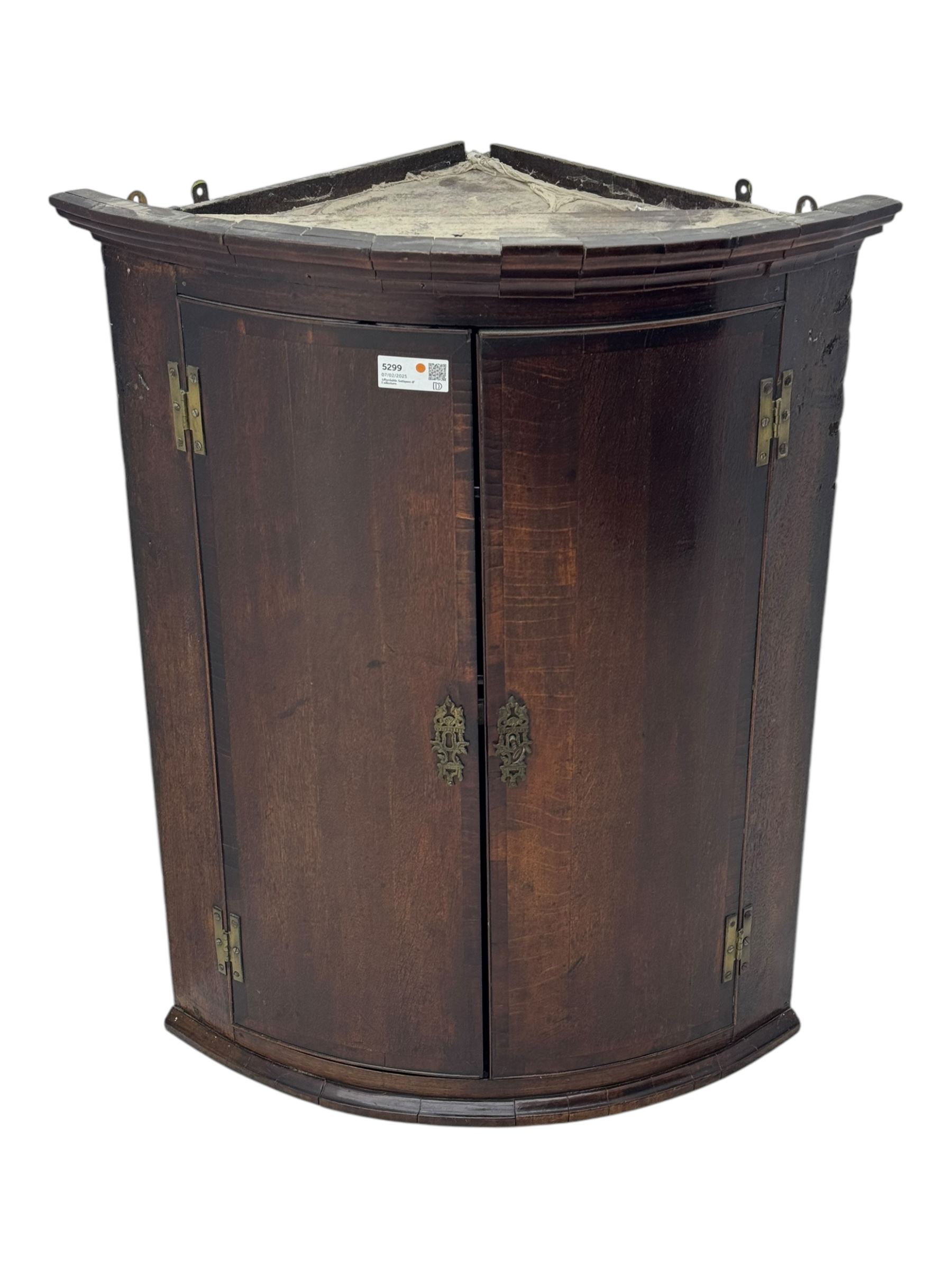 Early 19th century oak bow fronted wall hanging corner cupboard, projecting cornice over double doors enclosing shelving, on plinth base 