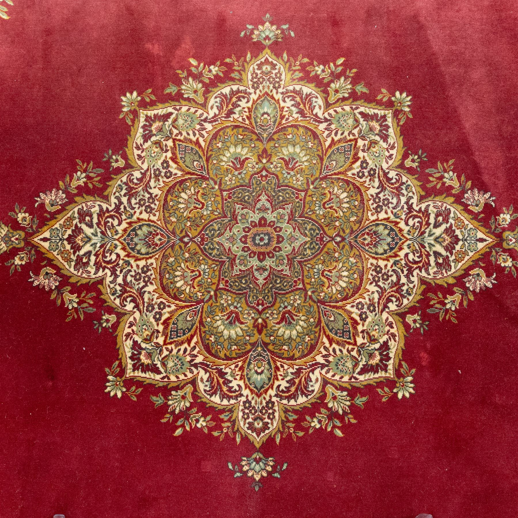 Kashan design carpet, crimson field with central medallion and scrolling floral sprays, cream and polychrome palmette and scrolling vine borders  
