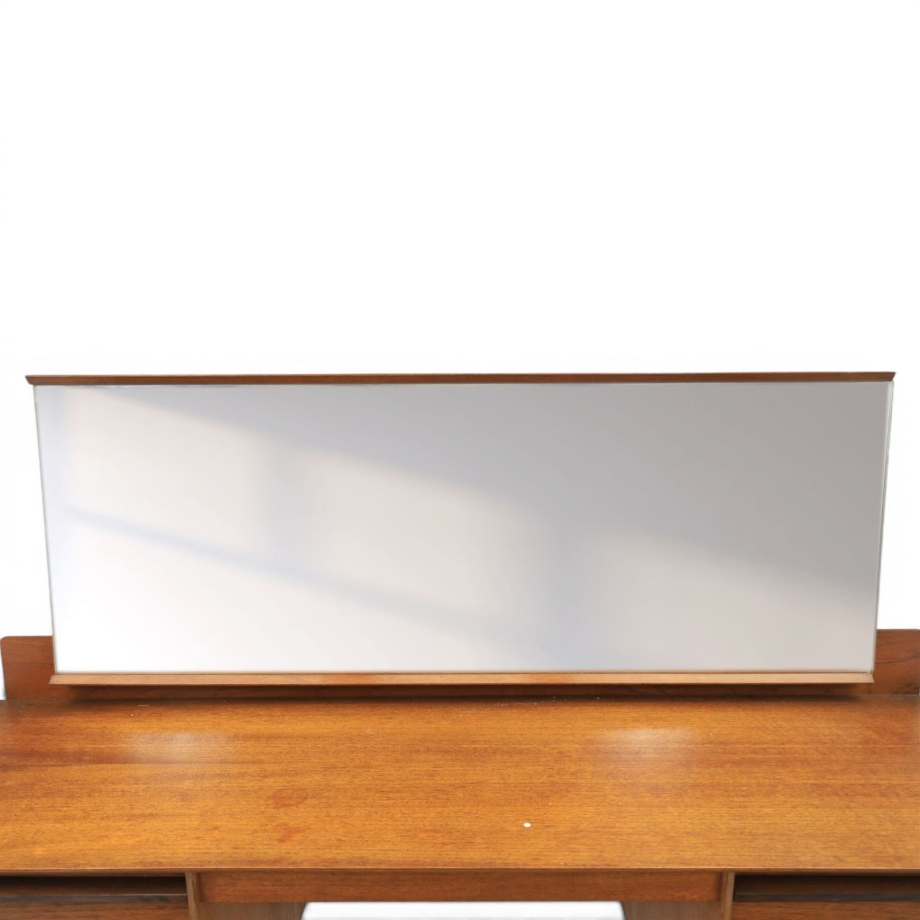 Austinsuite - mid 20th century teak headboard with bedside cabinets and matching  mirrored dressing table, the headboard with floating single drawer bedsides raised on a single tapering support, the dressing table with attached tilting mirror, above rectangular top with kneehole and two banks of two drawers, raised on tapering supports

Headboard H 84cm, D 40cm, W 229cm, W between bedsides 151cm 
Dressing table H 113cm D 44cm, W 149cm, H to underside of dresser 61cm