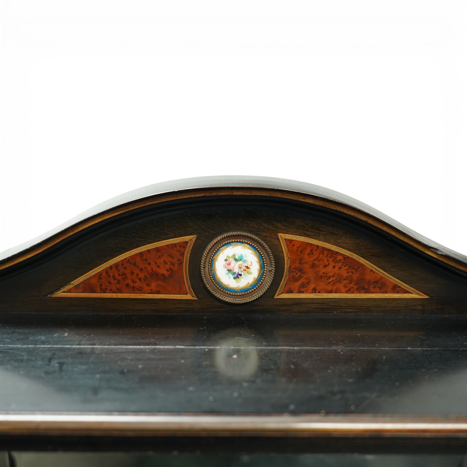Victorian Aesthetic Movement amboyna and ebonised cabinet, the arched raised back inlaid with amboyna and floral porcelain plaque, over a raised shelf with fluted and turned supports, and a bevelled mirror plate with brass beading beneath, the inverted-breakfront top over an ornate frieze drawer with guilloche style gilt-metal mounts and porcelain plaques, the panelled door with a central porcelain plaque depicting a lady in a fuchsia gown within concentric ebonised and amboyna inlays, flanked by architectural style uprights with Corinthian capitals, raised on turned feet