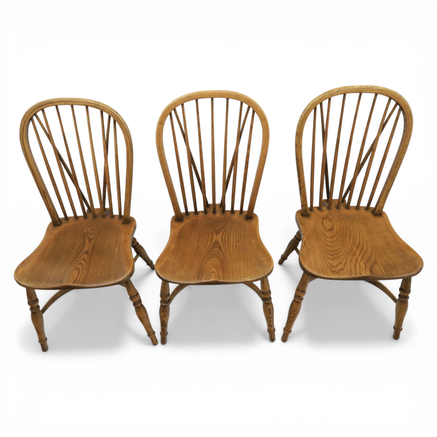 Traditional elm and beech Windsor dining chairs, each with hoop back and turned spindles over a shaped solid seat fitted with loose floral upholstered cushions, raised on turned tapering supports united by crinoline stretchers